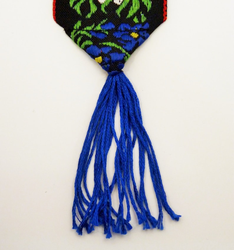May include: A blue tassel hangs from a black and green fabric bookmark with a floral pattern.