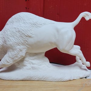 May include: A white ceramic figurine of a charging bull in a dynamic pose. The sculpture features detailed fur texture on the head and shoulders, a raised tail, and a sturdy base. The surface is matte white, highlighting the muscular form of the animal.