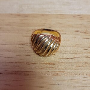Puede incluir: Un anillo de oro con un dise&ntilde;o acanalado. El anillo est&aacute; sobre una superficie de madera marr&oacute;n claro. El anillo est&aacute; marcado "14K".