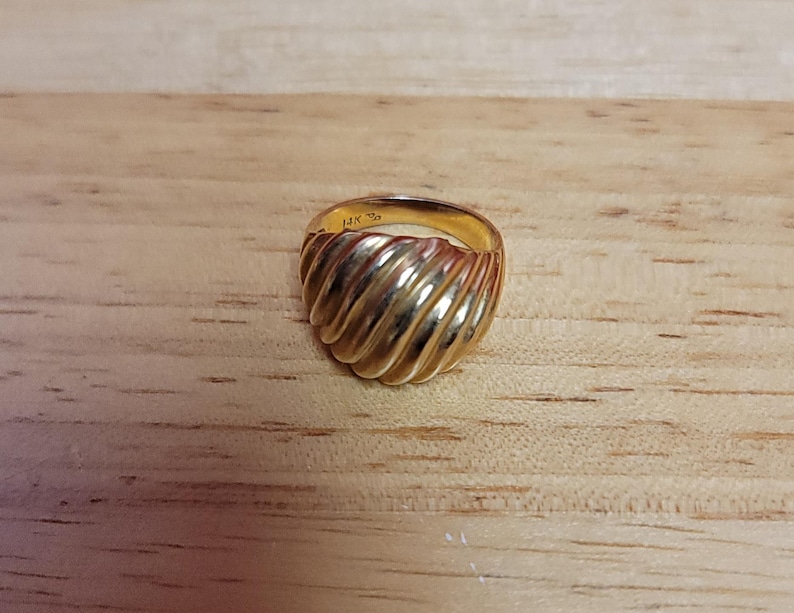 Puede incluir: Un anillo de oro con un dise&ntilde;o acanalado. El anillo est&aacute; sobre una superficie de madera marr&oacute;n claro. El anillo est&aacute; marcado "14K".