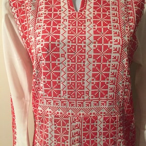 May include: White long-sleeved shirt with a red embroidered pattern. The embroidery features a geometric design with small red squares and diamonds.