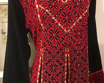 May include: A black long-sleeved dress with red embroidery and gold trim. The embroidery features a floral pattern with small silver beads.