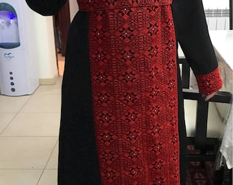 May include: A long black dress with red embroidered detailing. The embroidery features a geometric pattern with black and white accents.