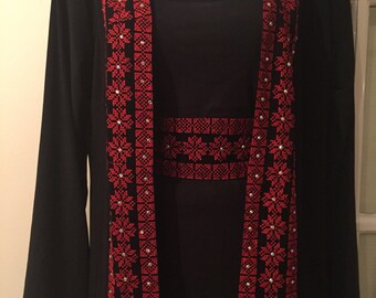 May include: A black abaya with long sleeves and a red embroidered design. The embroidery features a geometric pattern with small white beads.