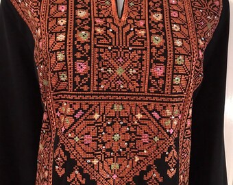 May include: Black long-sleeved dress with intricate embroidery in shades of brown, pink, and green. The embroidery features geometric patterns and small embellishments. The dress has a keyhole neckline and is displayed on a mannequin.