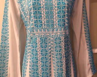 May include: A white dress with a turquoise embroidered pattern. The embroidery is a geometric design with squares and diamonds.