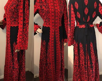 May include: A long black dress with red embroidery and a decorative beaded trim. The dress has a high neckline and long sleeves. The dress is open in the front and has a tie at the waist.