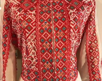 May include: White embroidered blouse with red, blue, and green geometric patterns. The blouse has a high collar and long sleeves.