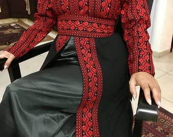 May include: A black maxi dress with a red embroidered bodice and long sleeves. The dress has a slit in the front and a belt at the waist.