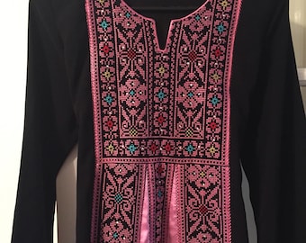 May include: Black long-sleeved dress with pink embroidery featuring floral and geometric patterns. The embroidery is detailed with colorful beads.