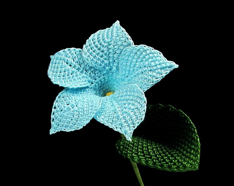 Peut inclure: Une fleur bleue en crochet avec une feuille verte en crochet. La fleur a un design &agrave; cinq p&eacute;tales et un centre jaune.