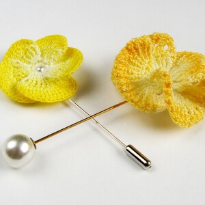 May include: Two yellow crocheted flower brooches with pearl centers attached to gold pins.