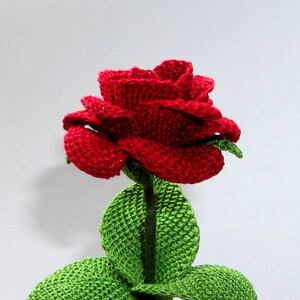 May include: A crocheted red rose with green leaves. The rose is made with yarn and has a realistic appearance.