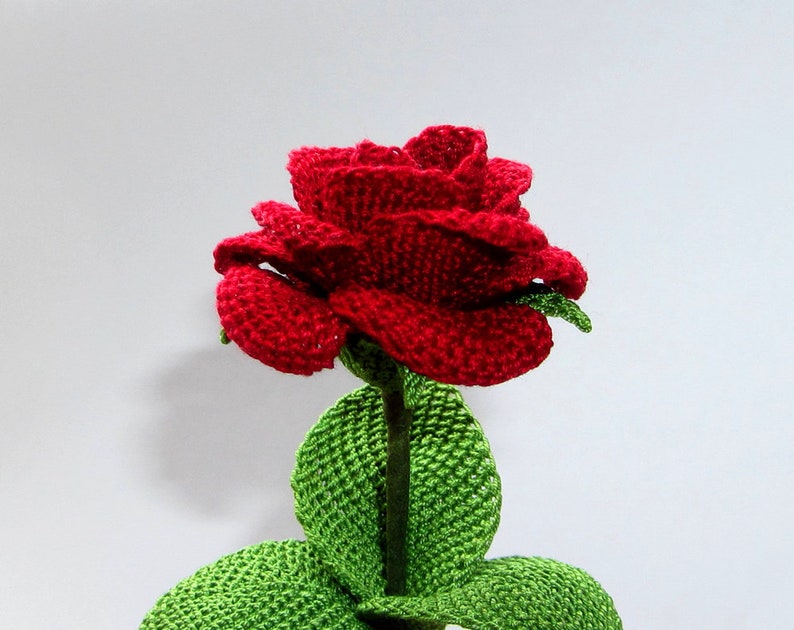 May include: A crocheted red rose with green leaves. The rose is made with yarn and has a realistic appearance.