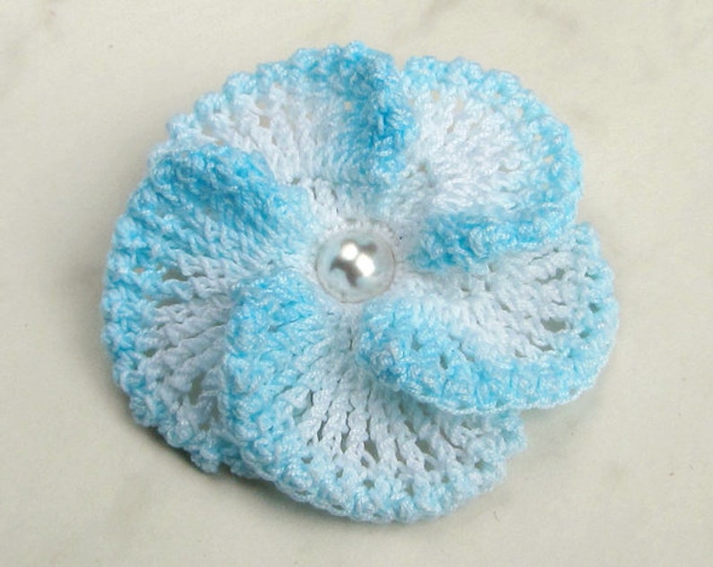 May include: A blue and white crocheted flower with a pearl-like button in the center.