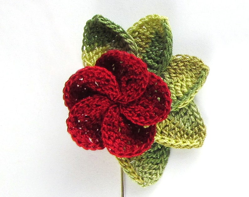 May include: A red crocheted flower with green crocheted leaves. The flower is a five-petal design and the leaves are a four-petal design.