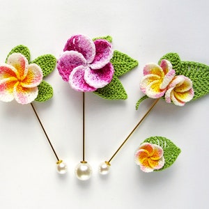 May include: Three crocheted flower pins with pearl heads. The flowers are pink, yellow, and white with green leaves.