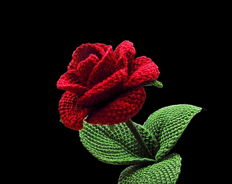 May include: A crocheted red rose with green leaves. The rose is made with yarn and is a handmade craft.