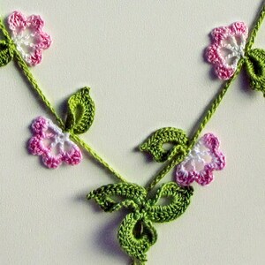 Puede incluir: Un collar hecho a mano de ganchillo con un delicado dise&ntilde;o floral. El collar tiene una vid verde con flores rosas y blancas y hojas verdes. El trabajo de ganchillo es intrincado y detallado, creando un accesorio encantador.