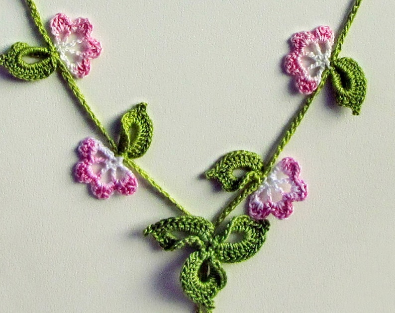 Puede incluir: Un collar hecho a mano de ganchillo con un delicado dise&ntilde;o floral. El collar tiene una vid verde con flores rosas y blancas y hojas verdes. El trabajo de ganchillo es intrincado y detallado, creando un accesorio encantador.