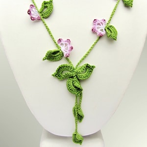 Puede incluir: Un collar de ganchillo hecho a mano con un dise&ntilde;o floral. El collar tiene vides verdes con hojas verdes y flores rosas y blancas. El collar se exhibe en un maniqu&iacute; blanco.