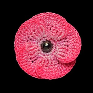 May include: A pink crocheted flower with a dark purple center bead.