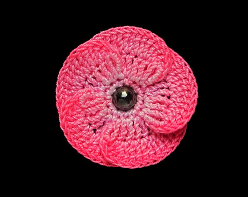 May include: A pink crocheted flower with a dark purple center bead.