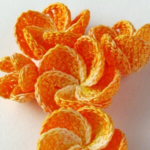 May include: A cluster of crocheted flowers in shades of orange and white. The flowers are made with a delicate, lacy stitch and have a slightly ruffled appearance.