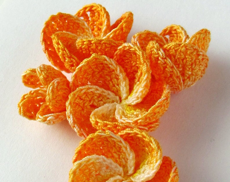 May include: A cluster of crocheted flowers in shades of orange and white. The flowers are made with a delicate, lacy stitch and have a slightly ruffled appearance.