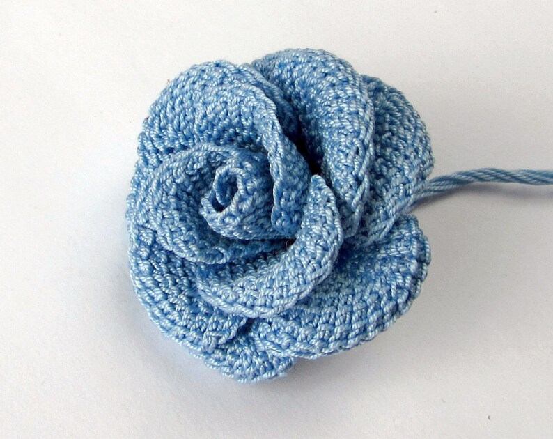 May include: A light blue crocheted rose flower with a single stem.