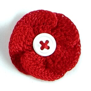 May include: A red crocheted flower with a white button in the center. The button has a cross design.