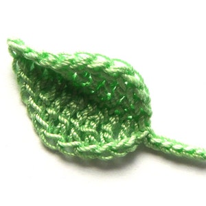 May include: A green crocheted leaf with a pointed tip and a stem. The leaf is made with a delicate stitch pattern.