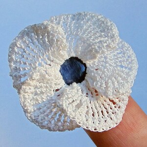 May include: A white crocheted flower with a blue center. The flower is small and delicate, and it is perfect for adding a touch of handmade charm to any project.