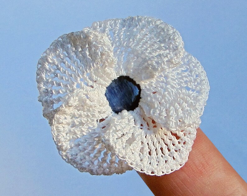 May include: A white crocheted flower with a blue center. The flower is small and delicate, and it is perfect for adding a touch of handmade charm to any project.