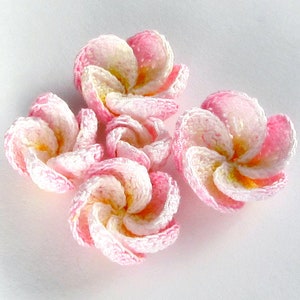 May include: Five crocheted pink and white flowers with a yellow center. The flowers are arranged in a cluster.