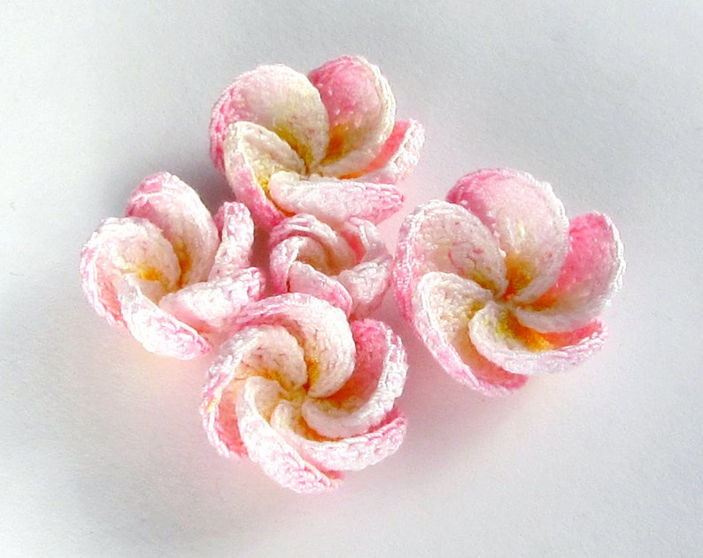 May include: Five crocheted pink and white flowers with a yellow center. The flowers are arranged in a cluster.