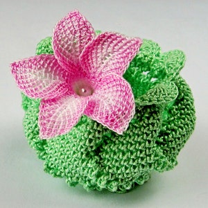 Peut inclure: Une fleur crochet&eacute; avec des p&eacute;tales roses et blancs, entour&eacute;e de feuilles crochet&eacute;es vertes.