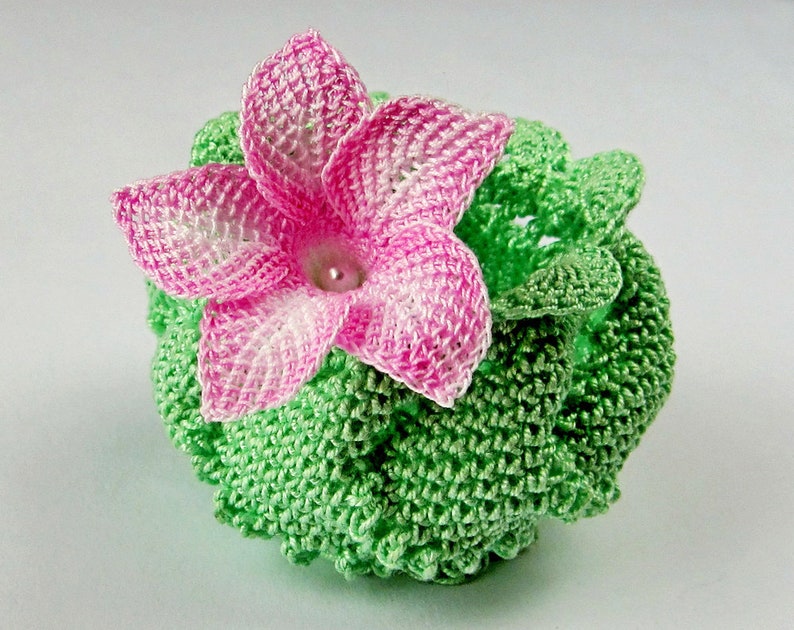 Peut inclure: Une fleur crochet&eacute; avec des p&eacute;tales roses et blancs, entour&eacute;e de feuilles crochet&eacute;es vertes.