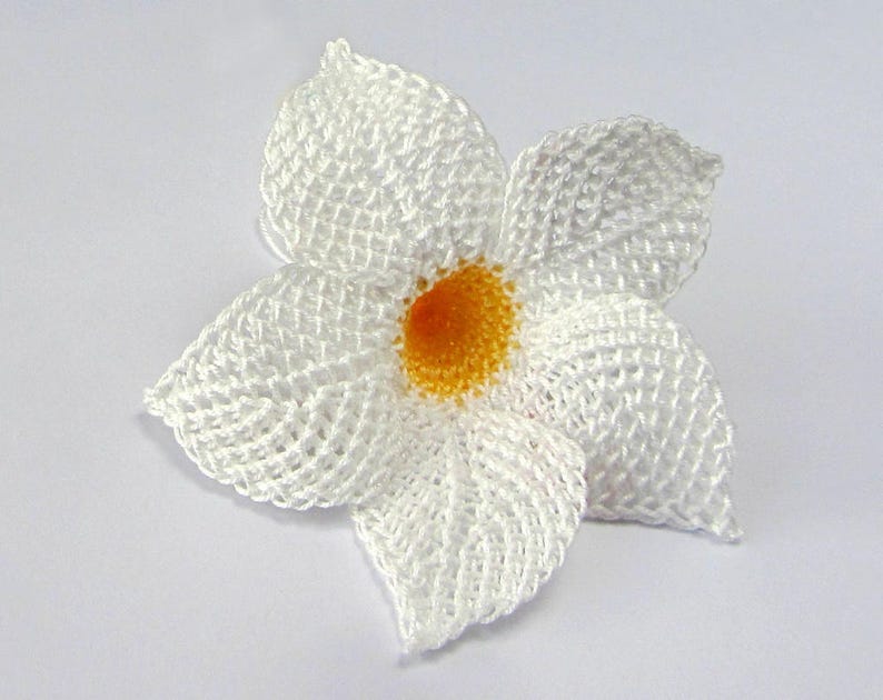 Peut inclure: Une fleur blanche en crochet avec un centre jaune. La fleur est faite de points d&eacute;licats et complexes et a une apparence d&eacute;licate et f&eacute;minine.