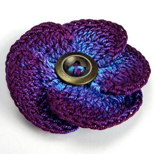 May include: A purple and blue crocheted flower with a large, round, brass button in the center.