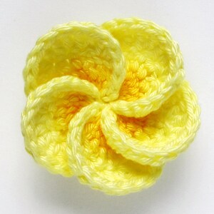 May include: A yellow crocheted flower with five petals. The flower is made with a light yellow yarn and has a slightly darker yellow center.