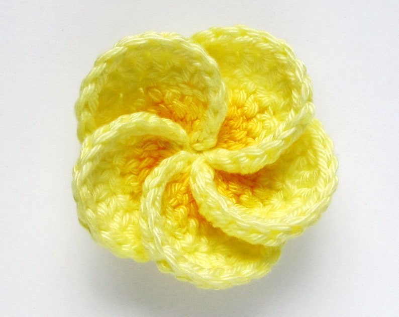 May include: A yellow crocheted flower with five petals. The flower is made with a light yellow yarn and has a slightly darker yellow center.