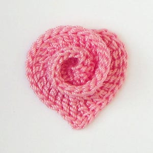 Peut inclure: Une fleur en crochet en forme de cœur de couleur rose avec un design en couches.