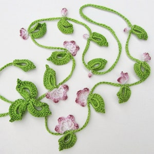 Puede incluir: Guirnalda floral de ganchillo con hojas verdes y flores rosas y blancas. La guirnalda est&aacute; hecha de hilo y tiene un aspecto artesanal. Adecuada para la decoraci&oacute;n del hogar o proyectos de manualidades. El dise&ntilde;o evoca enredaderas.