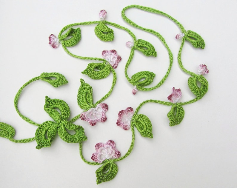 Puede incluir: Guirnalda floral de ganchillo con hojas verdes y flores rosas y blancas. La guirnalda est&aacute; hecha de hilo y tiene un aspecto artesanal. Adecuada para la decoraci&oacute;n del hogar o proyectos de manualidades. El dise&ntilde;o evoca enredaderas.