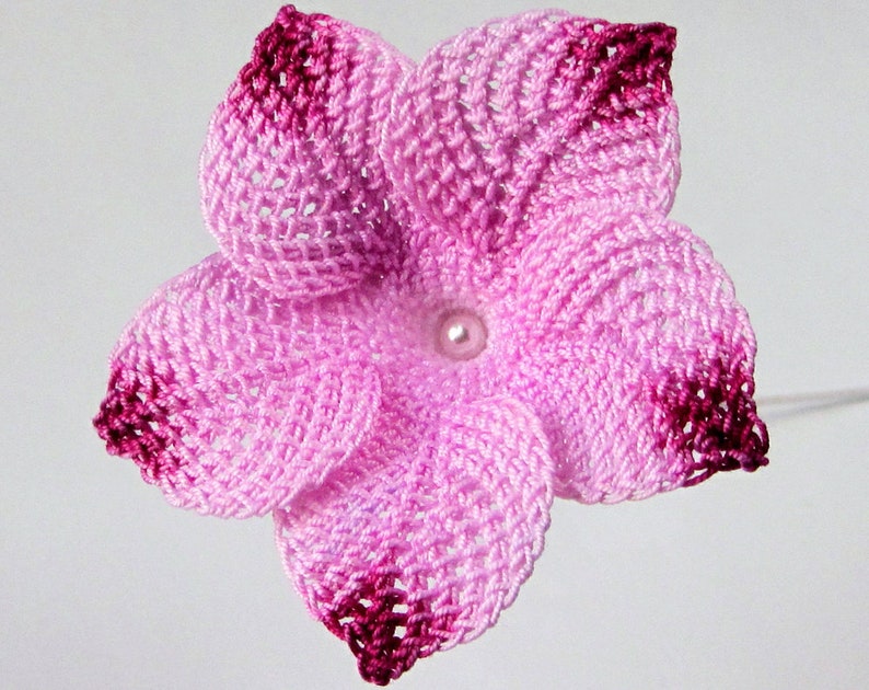 Peut inclure: Une fleur crochet&eacute; rose et bordeaux avec une perle au centre.