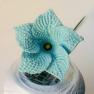 Peut inclure: Une fleur crochet&eacute; bleu clair avec un centre vert, pos&eacute;e sur une bobine de fil blanc.