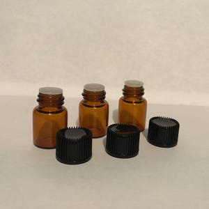 May include: Three amber glass bottles with white lids and black screw-on caps. The bottles are sitting on a white surface.