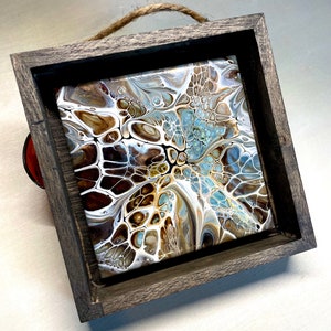 May include: A framed abstract painting with swirling patterns in shades of brown, white, and blue. The frame is made of dark wood and has a rustic look.