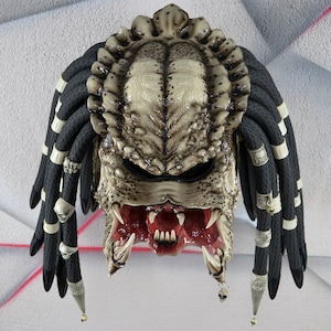 Puede incluir: Un casco de moto de estilo Predator blanco y negro con rastas. El casco tiene una m&aacute;scara facial detallada con dientes afilados y una boca roja.